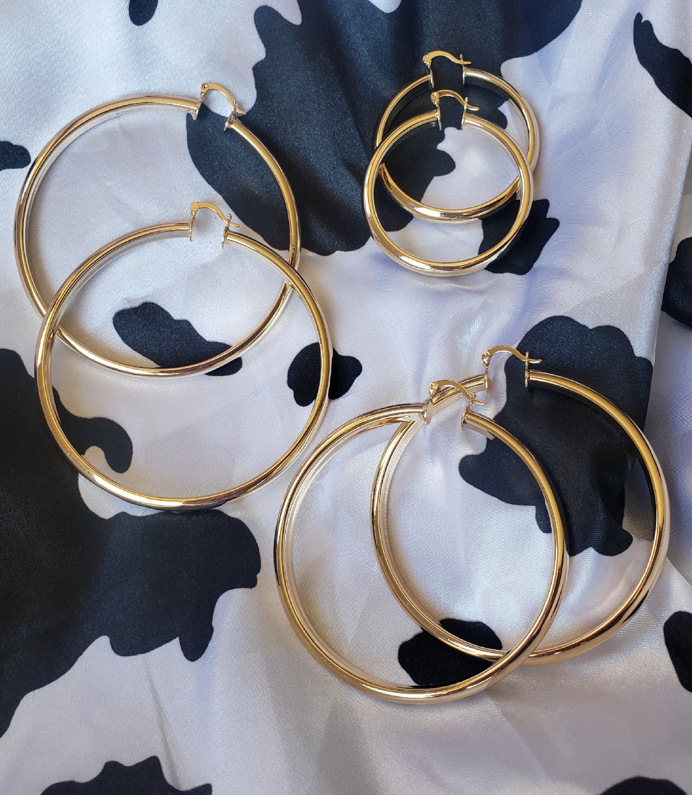 An array image of these gold plated vintage glam hoops. 3 sizes on a cow print silk background.