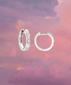 mini sterling silver diamond huggie earrings  product shoot on a pink and purple sky gradient backgraound